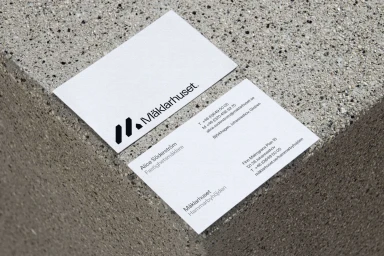Two white business cards with black typography resting on a textured grey stone surface.