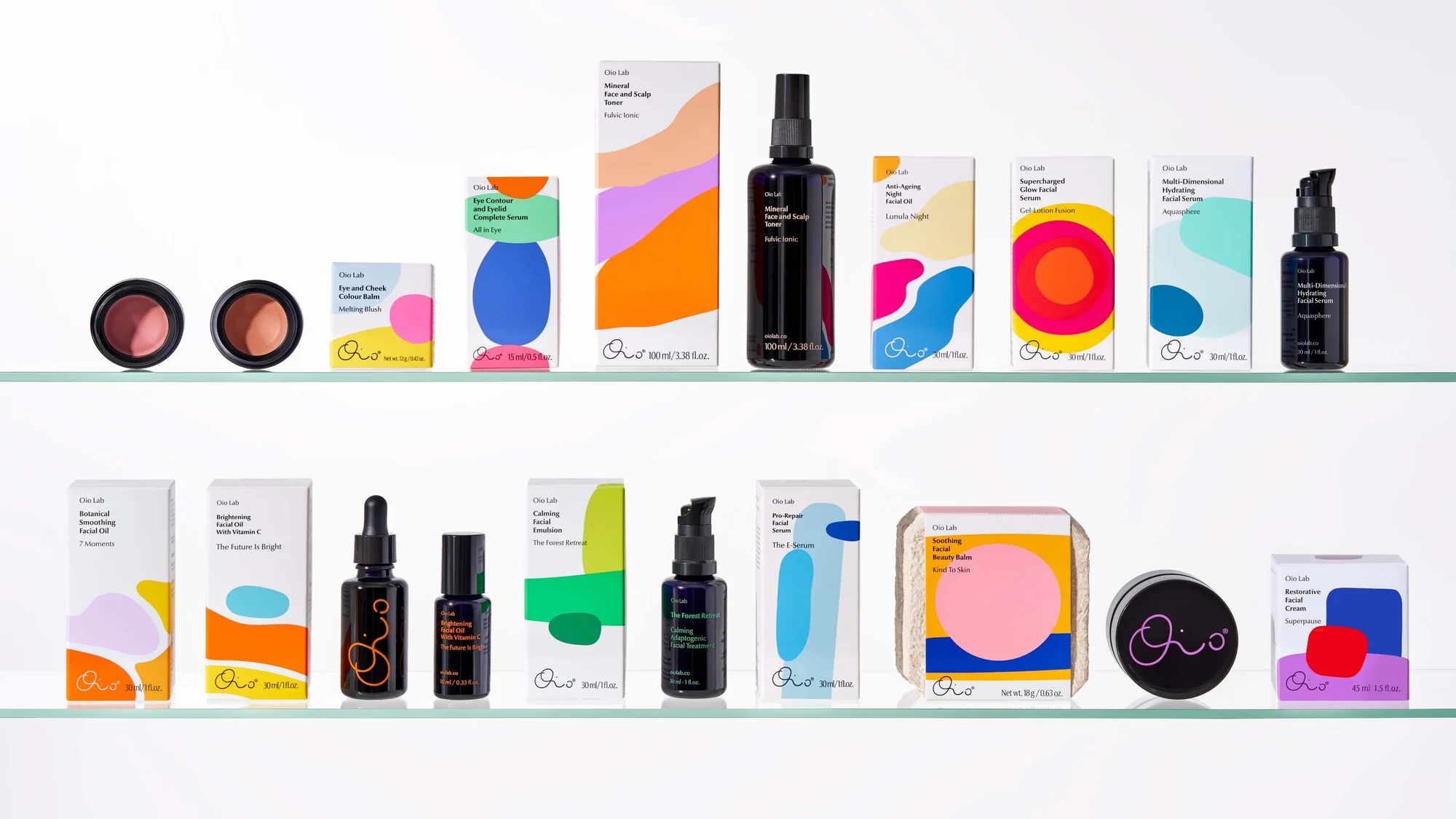 Assortment of Oio Lab skincare products in bottles, jars, and boxes arranged on glass shelves, featuring minimalist branding and colorful designs.