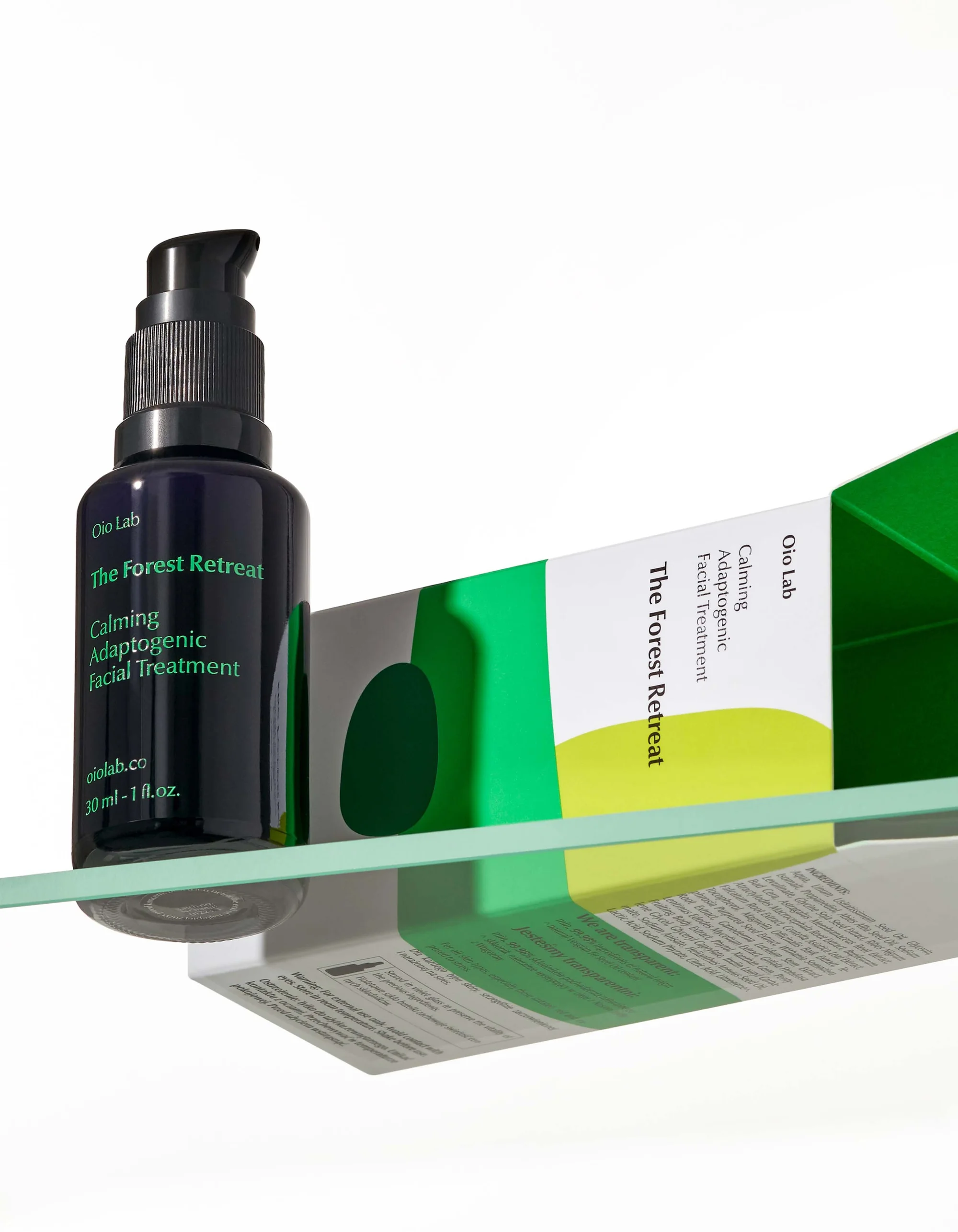 Serum bottle and box of The Forest Retreat Calming Adaptogenic Facial Treatment, from Qio Lab, sitting on a glass shelf in a studio.