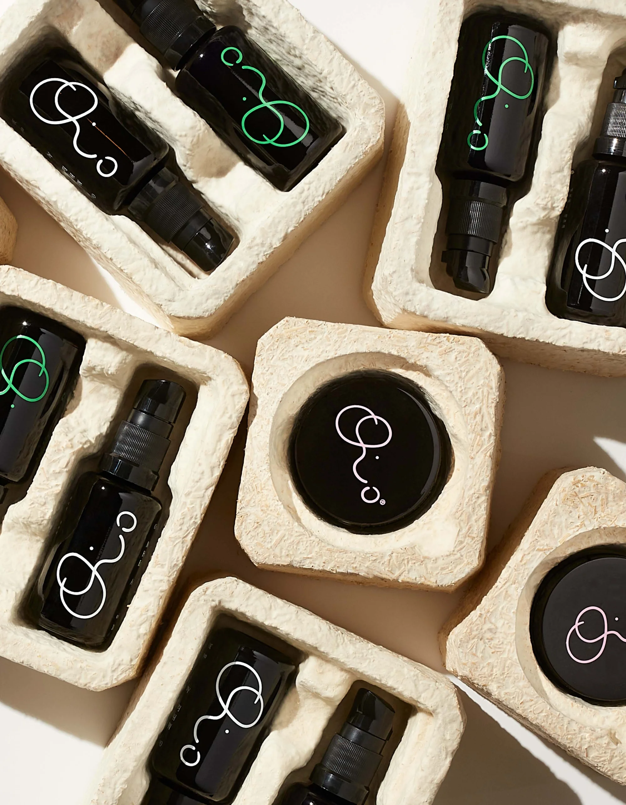 Overhead shot of black glass cosmetic bottles and jars in molded pulp packaging. Minimalist branding on dark containers.