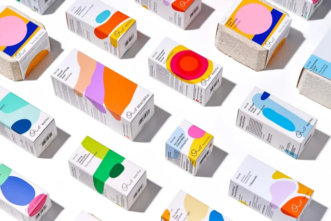 An overhead arrangement of colorful skincare product packaging boxes with abstract geometric shapes on a white background