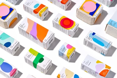 An overhead arrangement of colorful skincare product packaging boxes with abstract geometric shapes on a white background