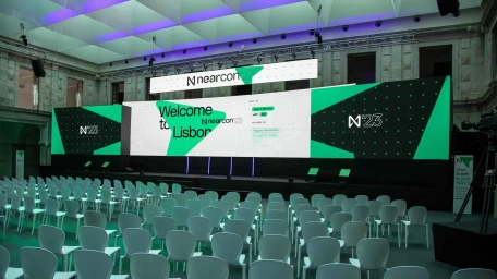 Wide conference hall featuring rows of white chairs facing a large stage with glowing green and white screens displaying text.
