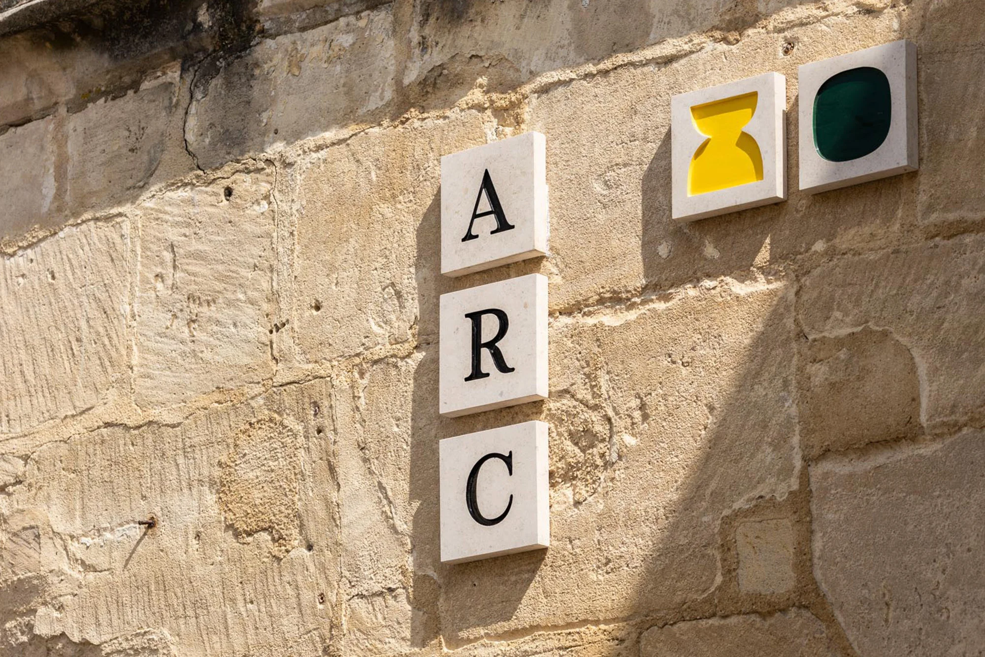 Sandstone wall with the letters ARC in stacked squares, plus two square art blocks with yellow and green geometric shapes.