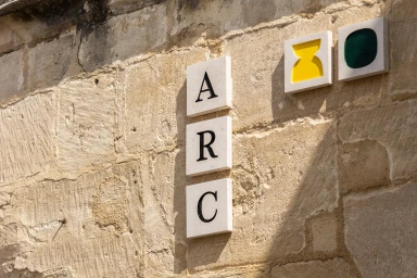 Textured stone wall displaying vertical white ceramic tiles with black typography spelling ARC and abstract icons.