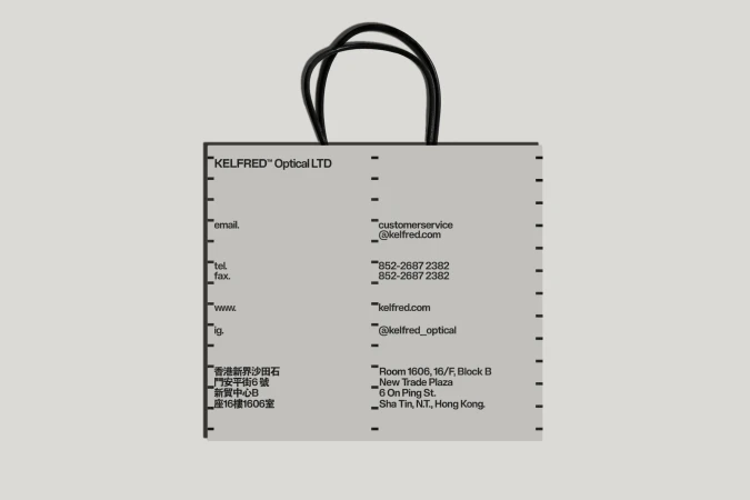 Kelfred Optical LTD branded shopping bag in light gray with contact details and logo, featuring black rope handles, studio lighting.