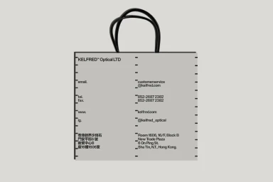 Grey paper shopping bag with black handles and typographic contact details for Kelfred Optical LTD