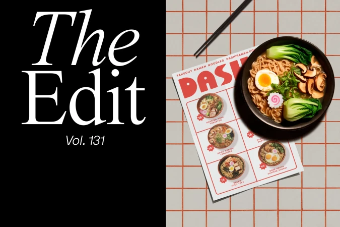 Overhead shot of a bowl of ramen with chopsticks and a menu on a checkered tile surface with a black background on the left.