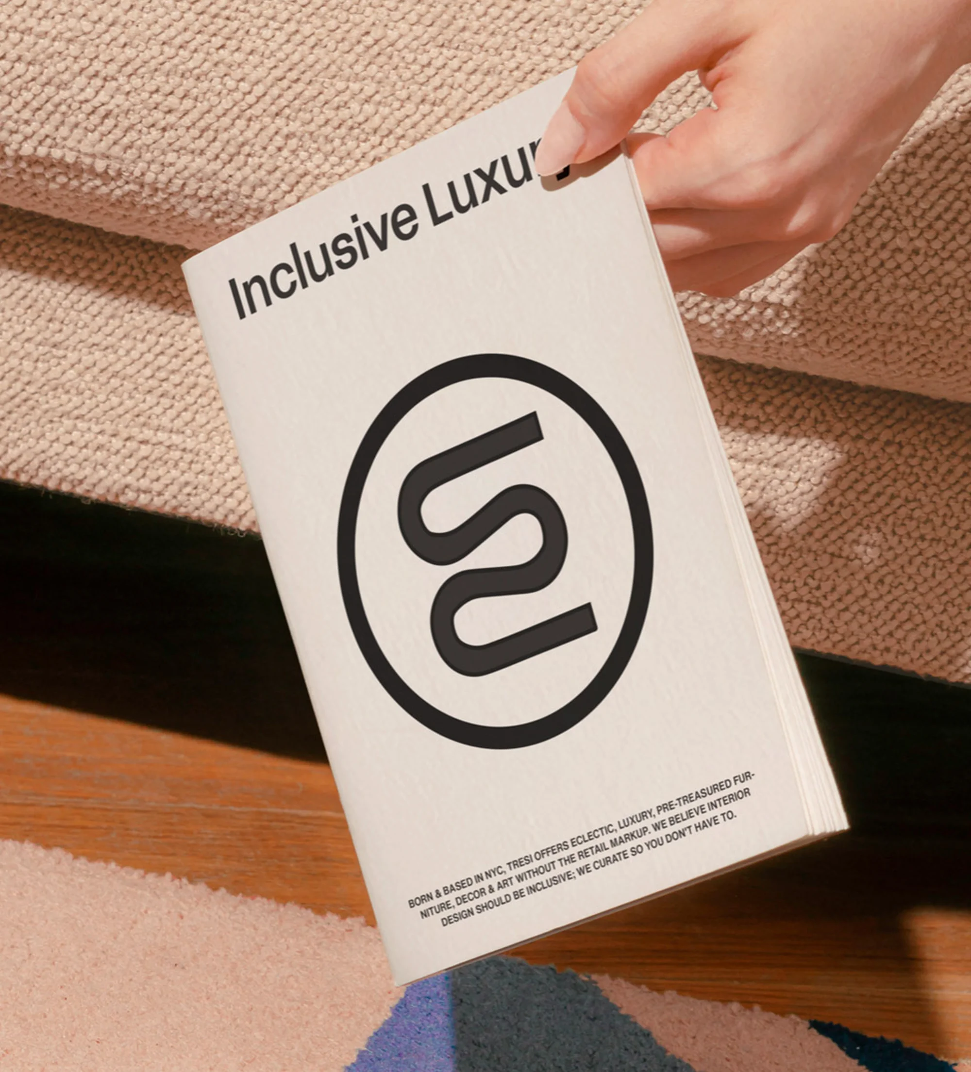 Close-up of a person holding a book with the text 'Inclusive Luxury' and a black and white logo on a beige surface.