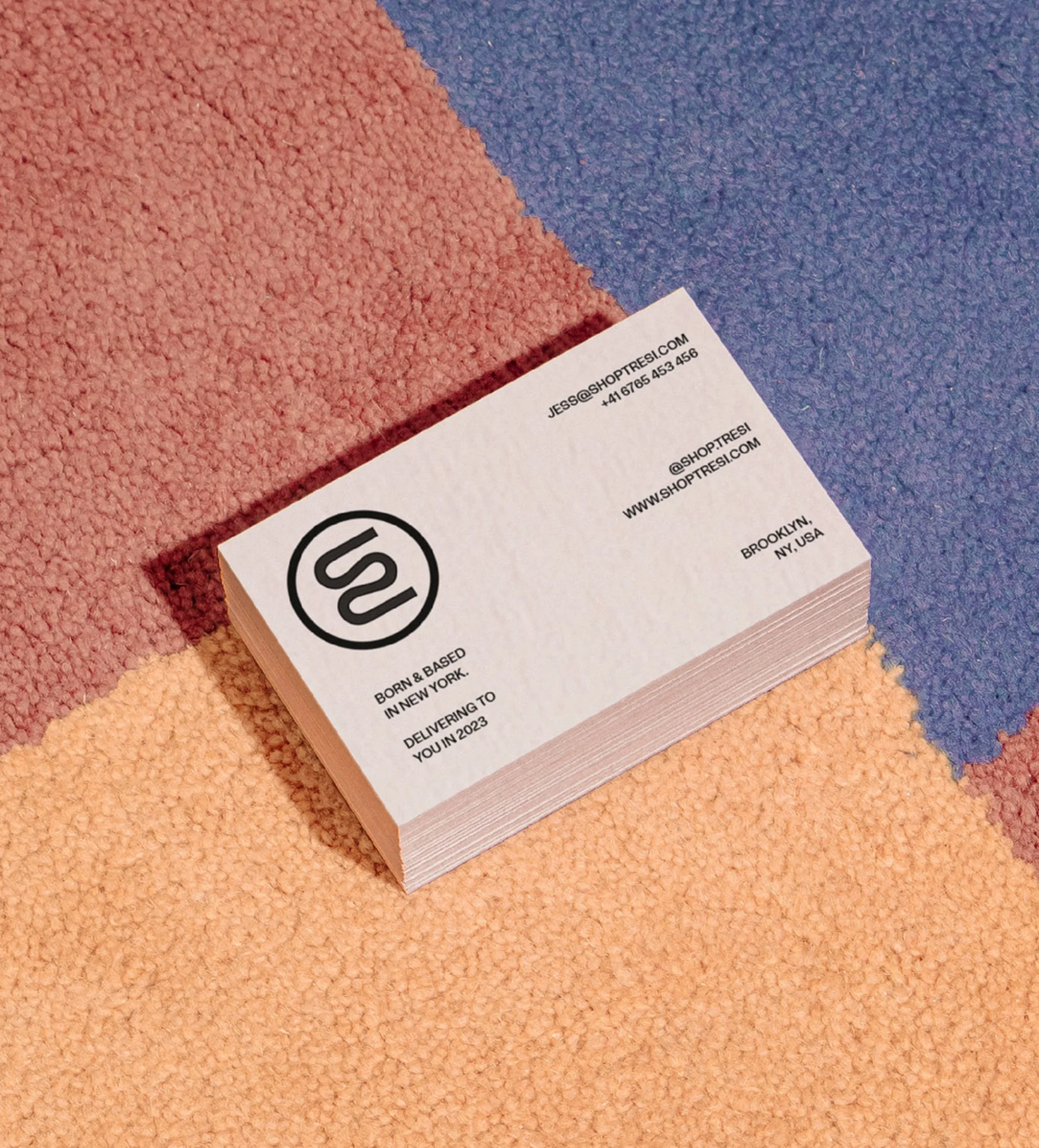 Stack of business cards on a multi-colored carpet. Business cards feature a logo and contact information against a carpet background.