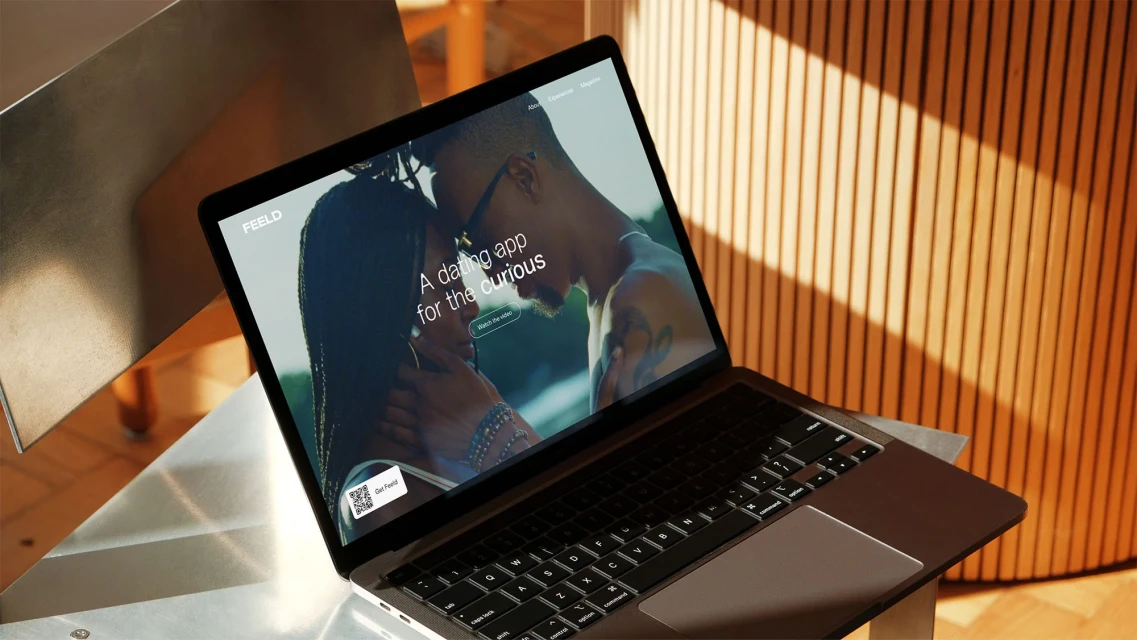 Laptop displays a dating app featuring a couple, set against a backdrop of warm wood paneling and geometric metal accents.