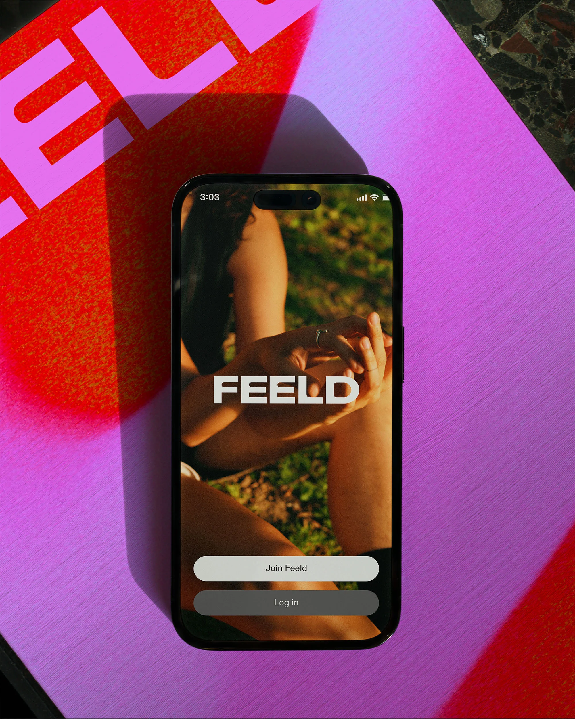 Smartphone displays the Feeld app interface on a violet surface with a red shadow; the screen shows a woman with green background.