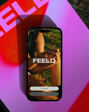 Smartphone displays the Feeld app interface on a violet surface with a red shadow; the screen shows a woman with green background.