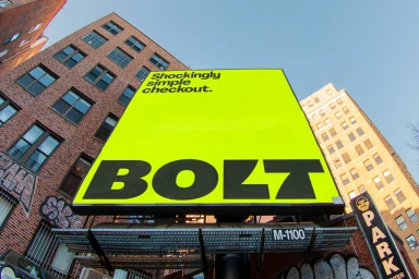 Low-angle outdoor shot of a bright lime-green billboard displaying bold black Bolt typography against a blue sky and brick buildings.