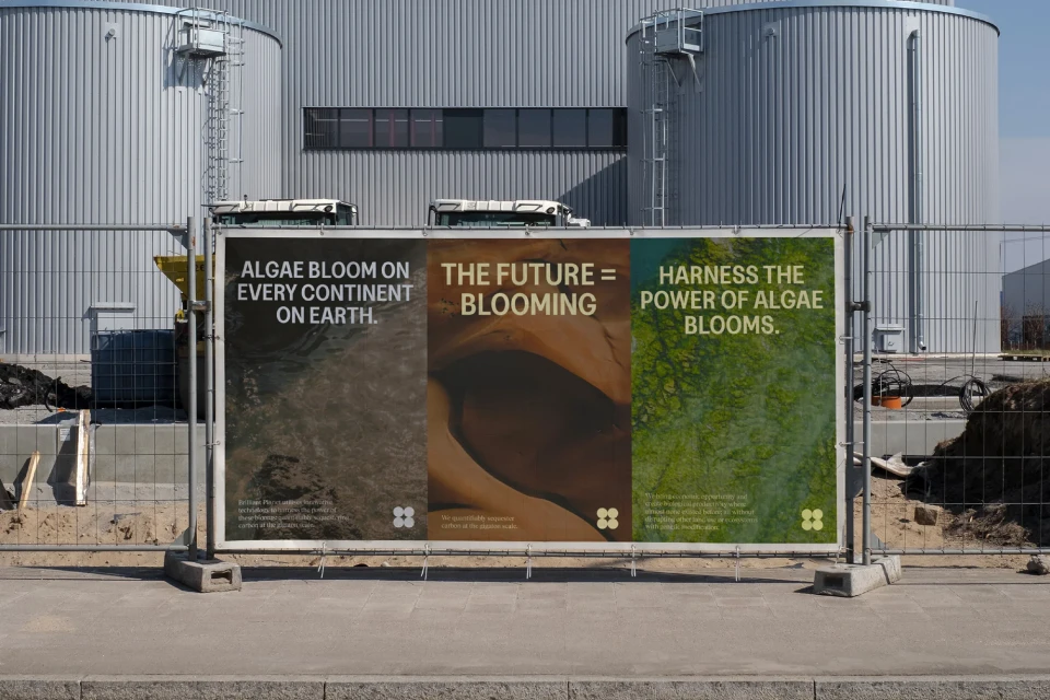 Outdoor view features three adjacent posters in metal frames displaying text and abstract algae imagery against an industrial background.