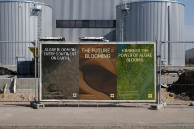 Large outdoor banner featuring three panels with environmental text mounted on a chain-link fence before industrial buildings