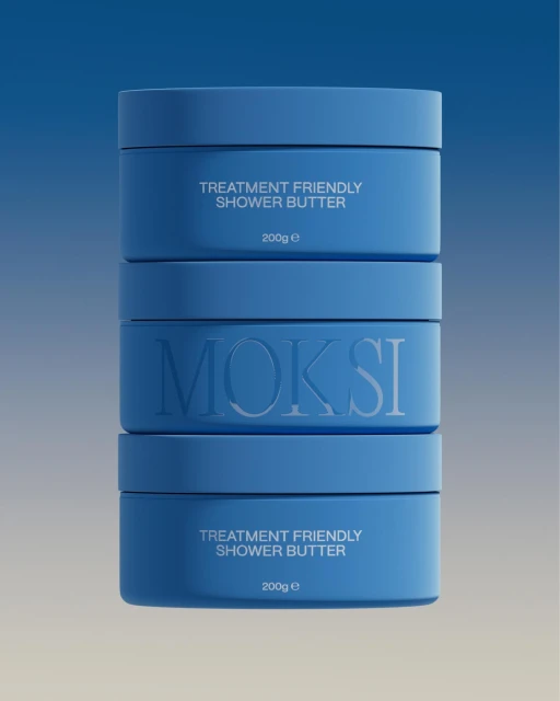 Stack of blue containers of MOKSI Treatment Friendly Shower Butter. Beauty and skincare product shot with solid studio lighting and minimal aesthetic.