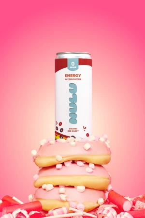 An energy drink can balanced vertically on a stack of three pink iced doughnuts against a monochrome pink studio background.