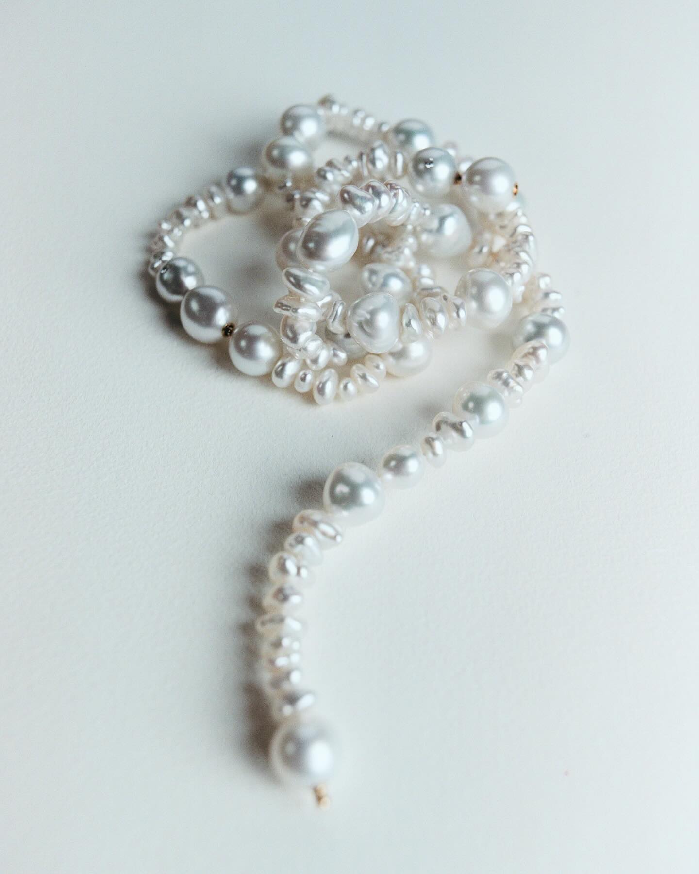 Close-up of a twisted strand of white pearls on a white background, featuring various sizes and shapes, with a focus on texture and detail.