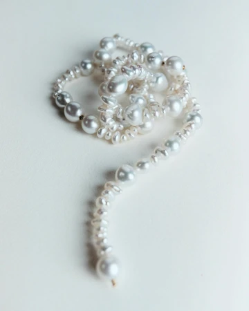 Close-up of a twisted strand of white pearls on a white background, featuring various sizes and shapes, with a focus on texture and detail.