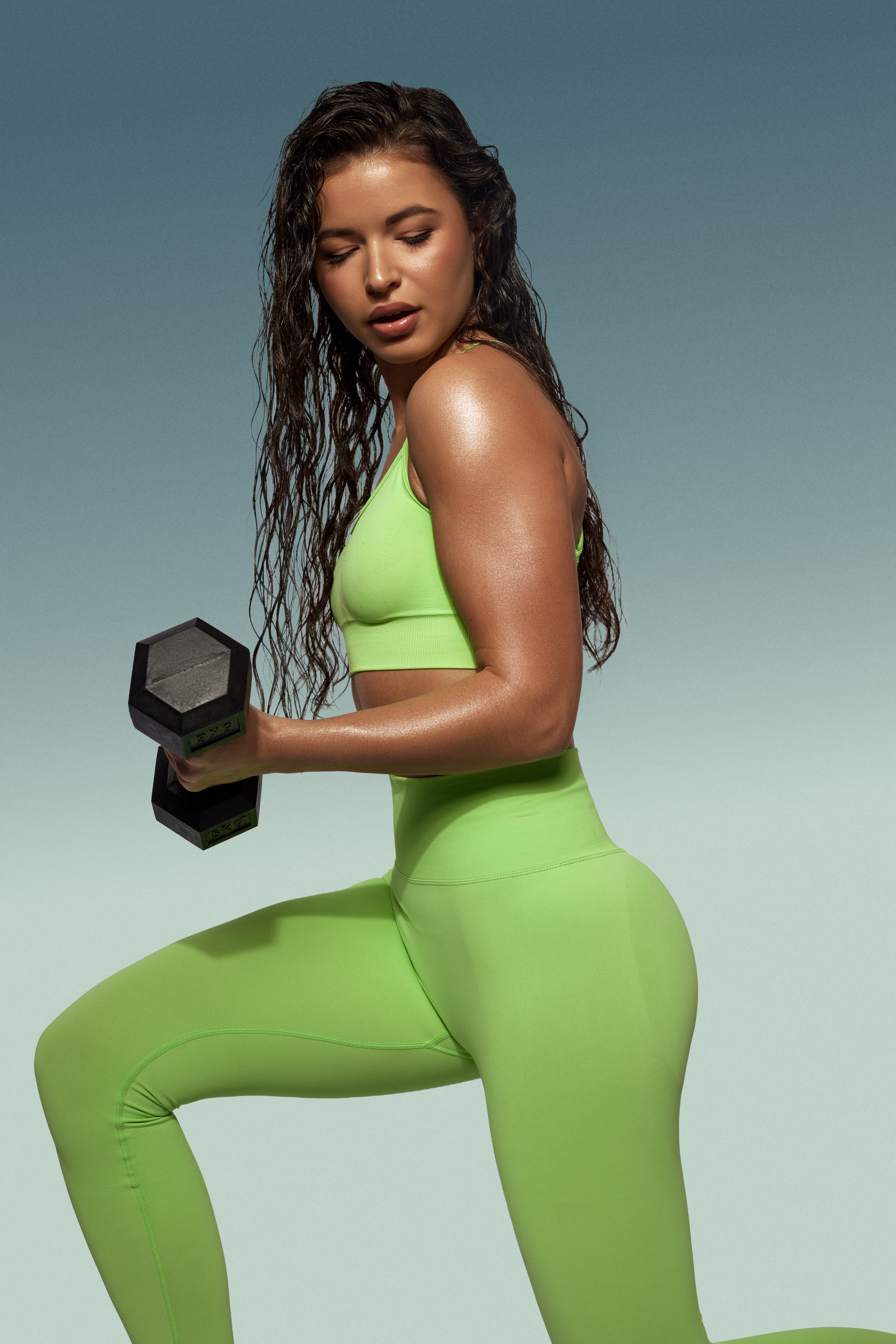 A woman in activewear does a dumbbell lunge, highlighting her fitness routine and athletic physique against a gradient backdrop.