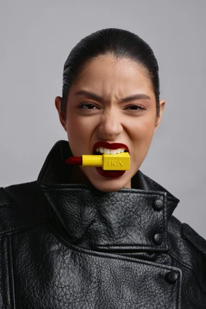 Close-up of a fierce woman in a leather jacket biting on a yellow lipstick. Bold beauty statement in a studio setting, featuring makeup.