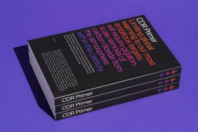 Three 'CDR Primer' books stacked, addressing carbon dioxide removal. Black covers with colorful text, shot in a studio on purple backdrop.