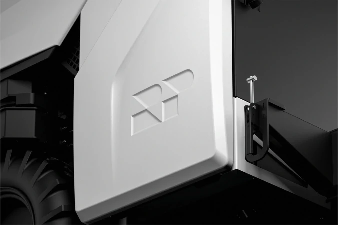 Close-up of a white autonomous vehicle featuring a tire and a geometric logo, set against a grey and black background.