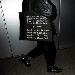 Person walking in dark clothing carrying a black tote bag with white text against metal panels