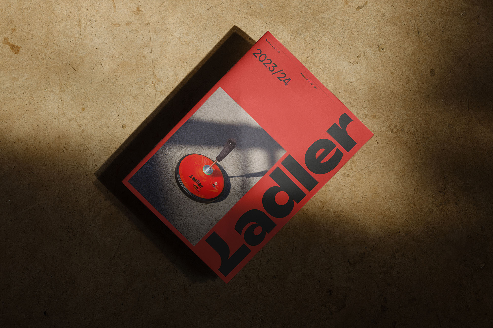 Overhead shot of a coral-colored magazine titled 'Ladler 2023/24' with an illustration of a cooking ladle on a speckled surface.