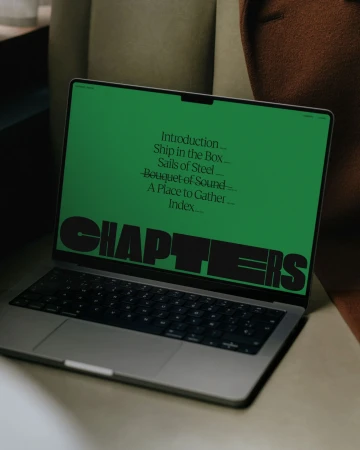 Silver laptop screen displays a green background with the word "CHAPTERS" and a table of contents listed on the screen.