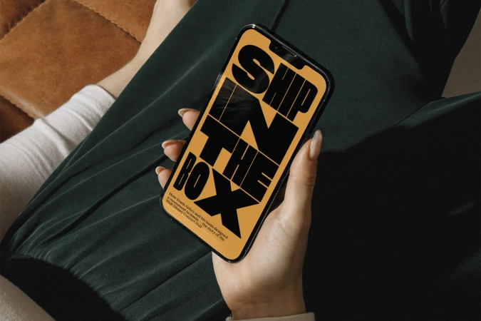 Close-up of a woman holding a black smartphone in her hand with a yellow screen displaying black graphic typography.