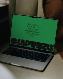 Laptop displaying a vibrant green screen with bold typography resting on a surface with a brown coat.