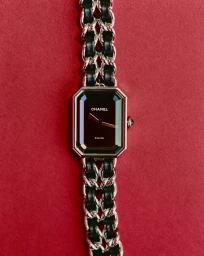 Close-up of a luxury wristwatch with an octagonal black dial and silver chain strap interwoven with leather against a textured red background