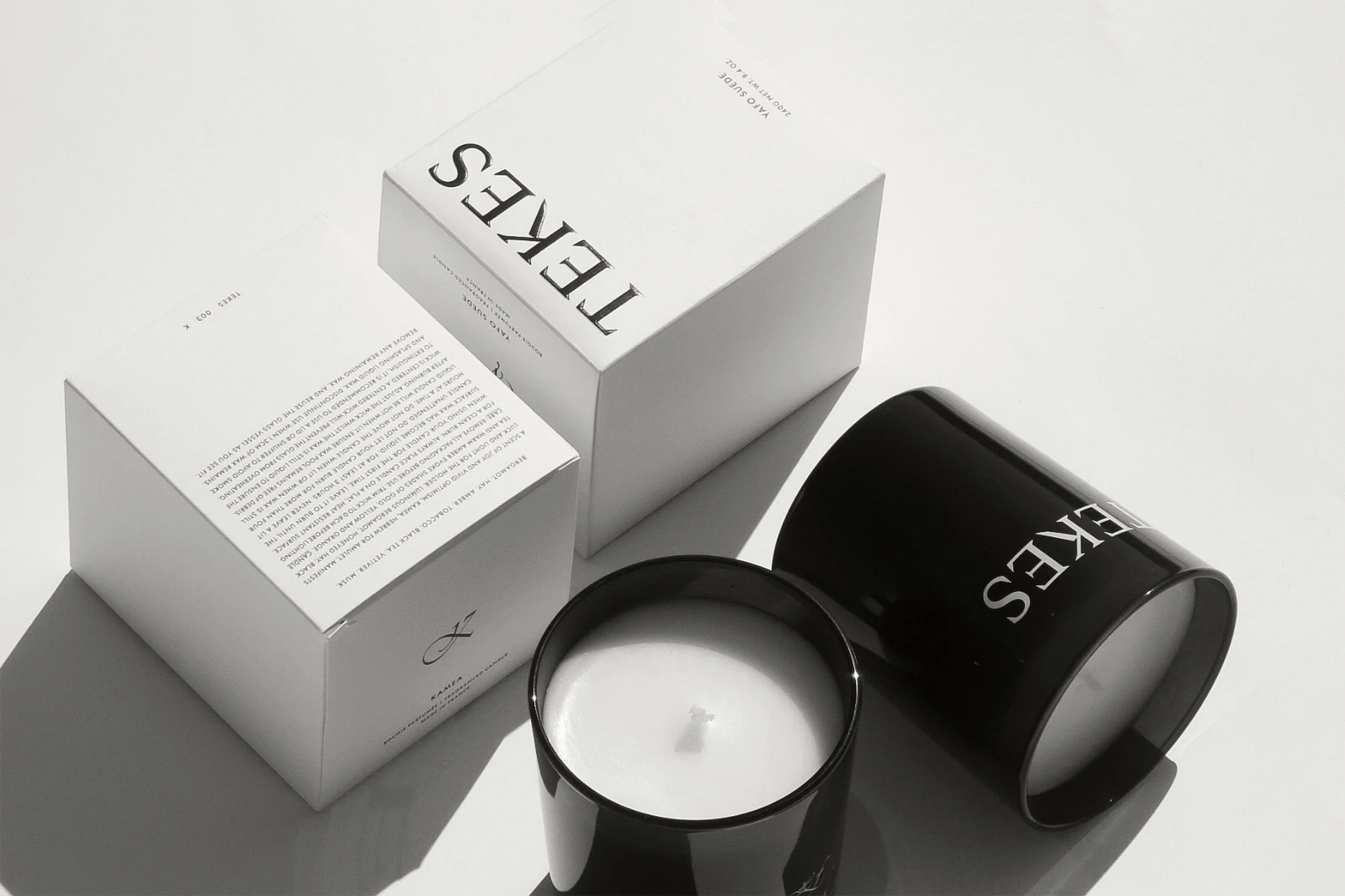 Two Tekes candles and boxes are arranged on a white surface in a minimalist style, evoking a sense of luxury and aromatic design.