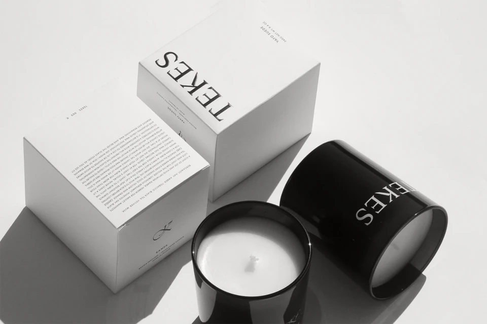 Two Tekes candles and boxes are arranged on a white surface in a minimalist style, evoking a sense of luxury and aromatic design.