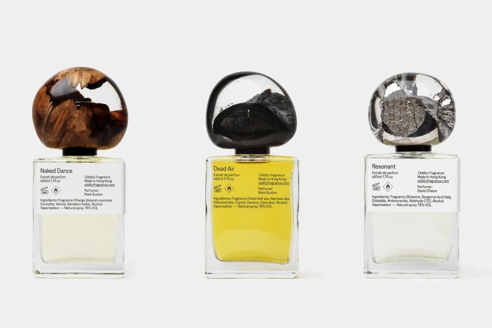 Three uniquely capped perfume bottles in a row on a neutral surface, each containing a different colored liquid.