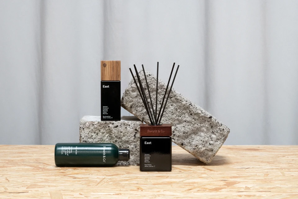 Still life of black fragrance bottles with wooden accents, arranged on a light wood surface against a gray and white backdrop.