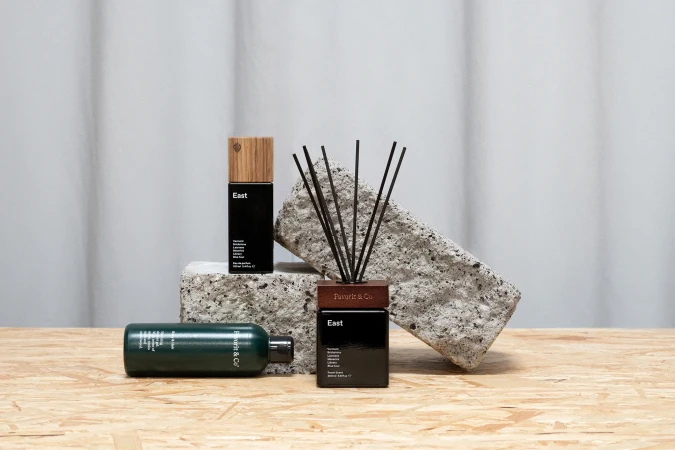 Still life of black fragrance bottles with wooden accents, arranged on a light wood surface against a gray and white backdrop.