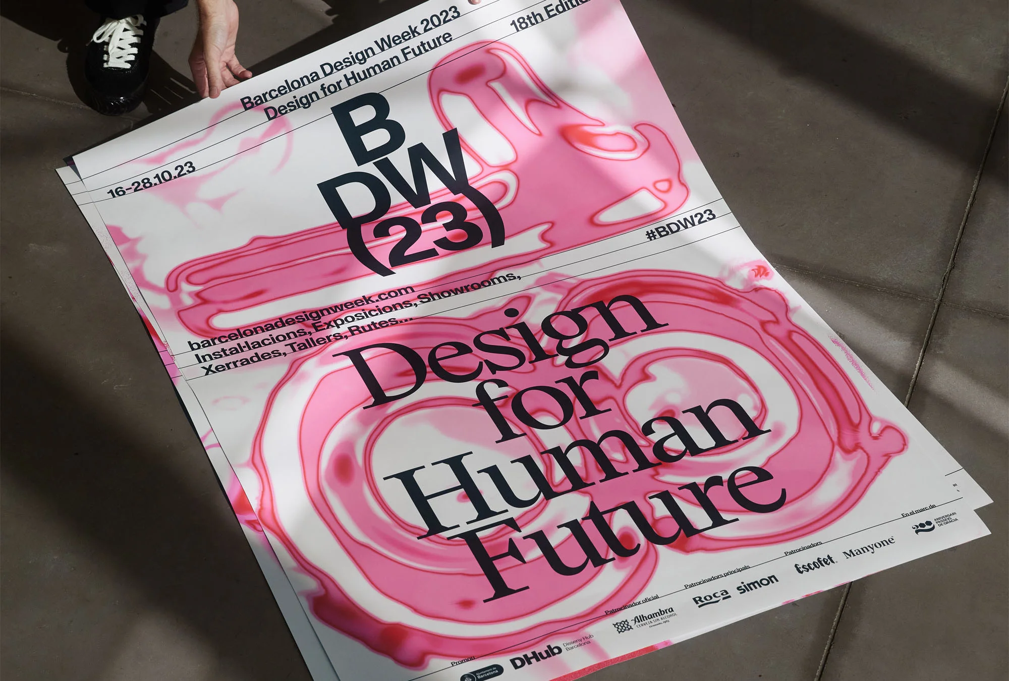 Close-up of Barcelona Design Week 2023 posters featuring pink liquid designs and event details, held by a person wearing black.