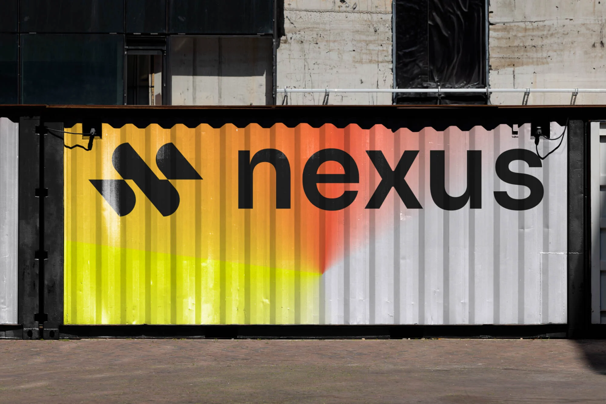 Black Nexus logo and wordmark on a metal shipping container with yellow, orange, and white spray paint and a concrete building background.