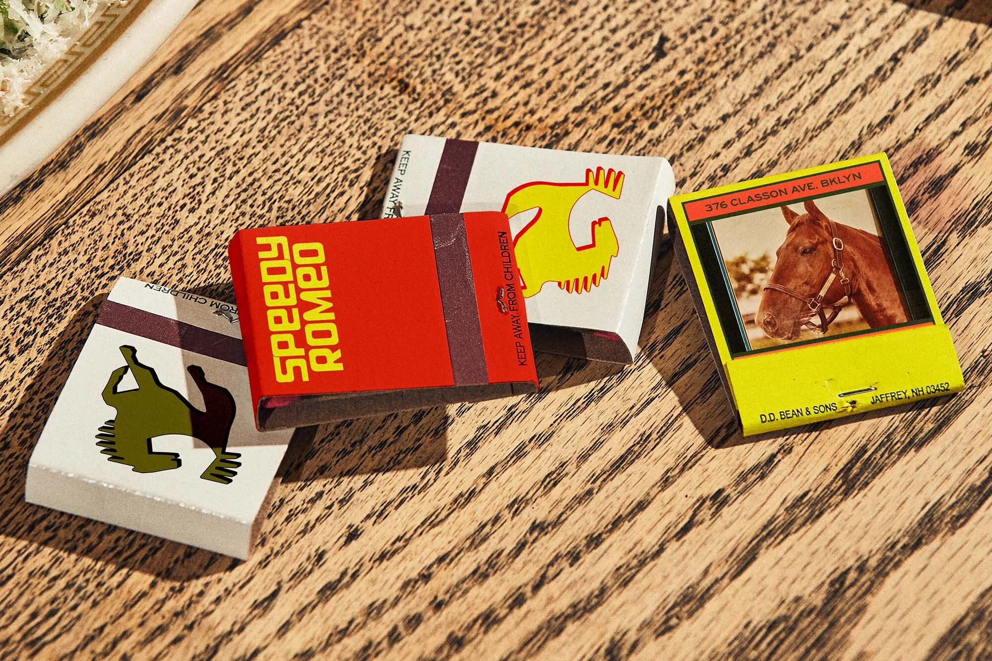 Close-up of matchboxes with colorful graphics and text on a wooden surface, creating a vintage and artistic composition.
