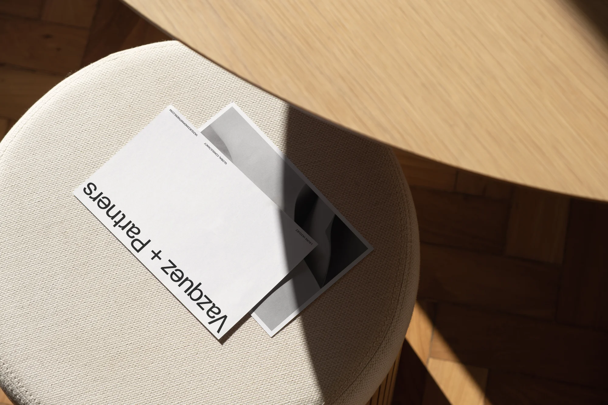 Overhead shot of two magazines on a padded stool near a wood table, casting a shadow on the stool and floor.