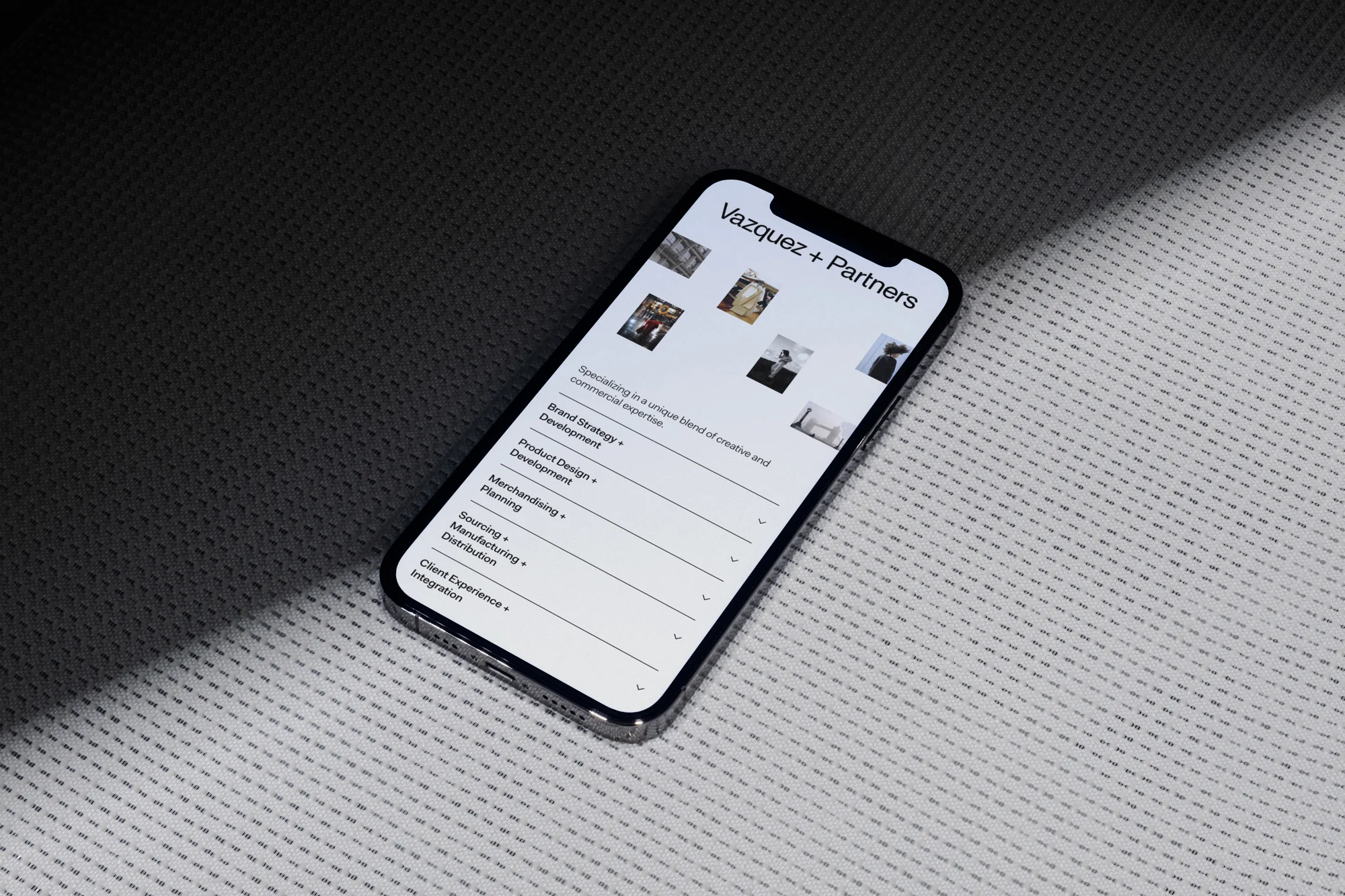 Smartphone displaying the website of Vazquez + Partners on a patterned surface with diffused lighting, creating a professional digital look.