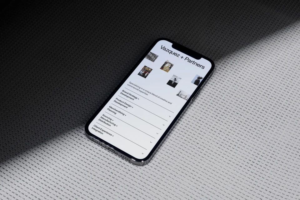 Smartphone displaying the website of Vazquez + Partners on a patterned surface with diffused lighting, creating a professional digital look.