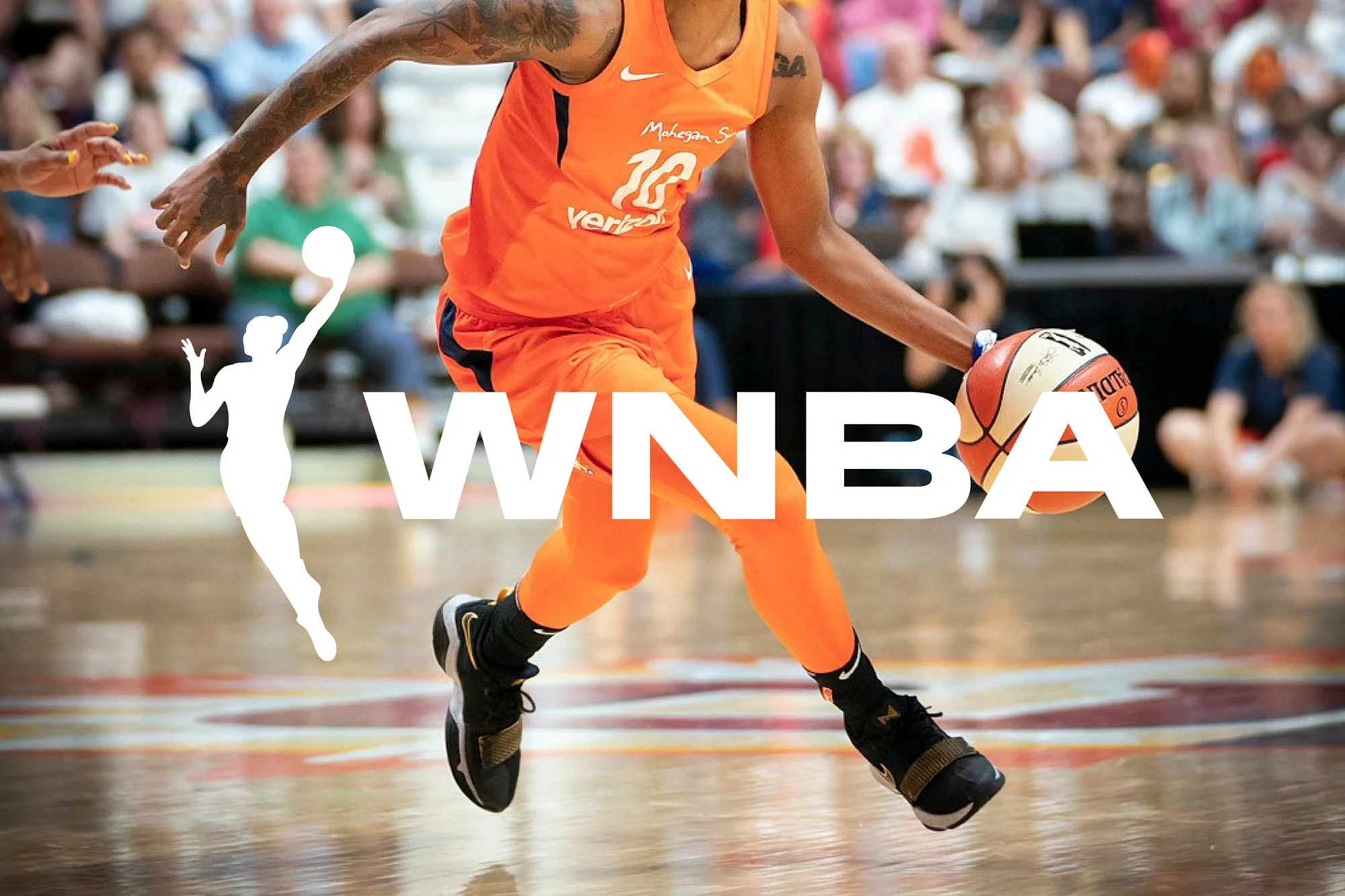 A female basketball player dribbles a ball in an indoor arena. She wears an orange uniform. The WNBA logo is superimposed.