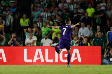 A soccer player in a purple number 7 jersey celebrates on the field in front of a large Laliga advertising board.