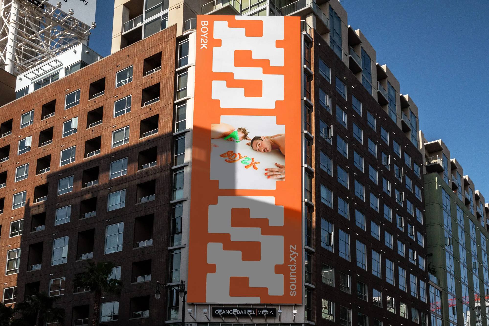 Billboard on building in urban setting showing two fair-skinned adults lying down near colorful starfish shapes with white and orange text.