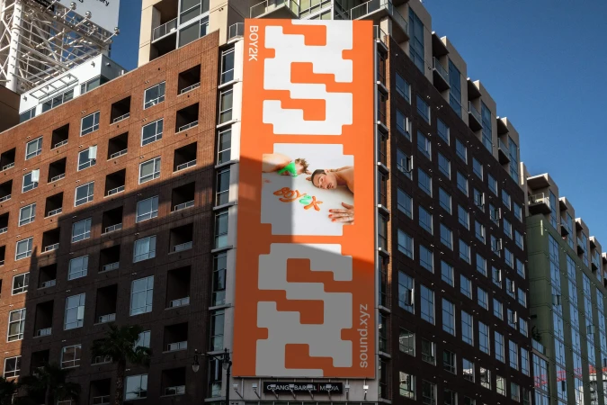 Billboard on building in urban setting showing two fair-skinned adults lying down near colorful starfish shapes with white and orange text.