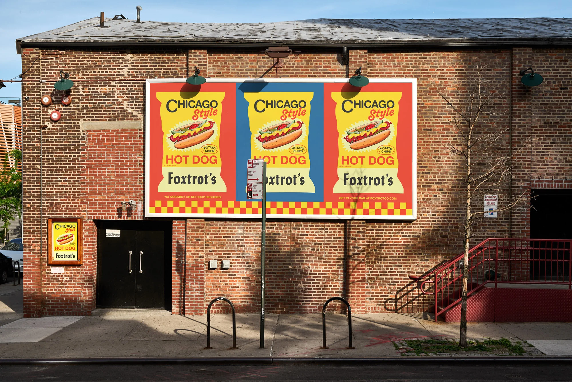 Outdoor shot of a brick building with a large billboard advertising Chicago Style Hot Dogs. Bike racks line the sidewalk in front.